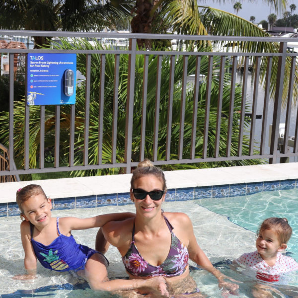 Mom and Kids Playing in Pool with TALOS Lightning Detector Sign in the Background
